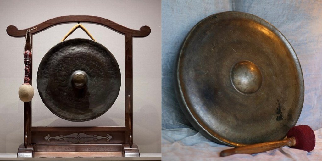 Two Chinese gongs. The one on the left is suspended from a frame. The one on the right is sitting on and leaning against cloth.