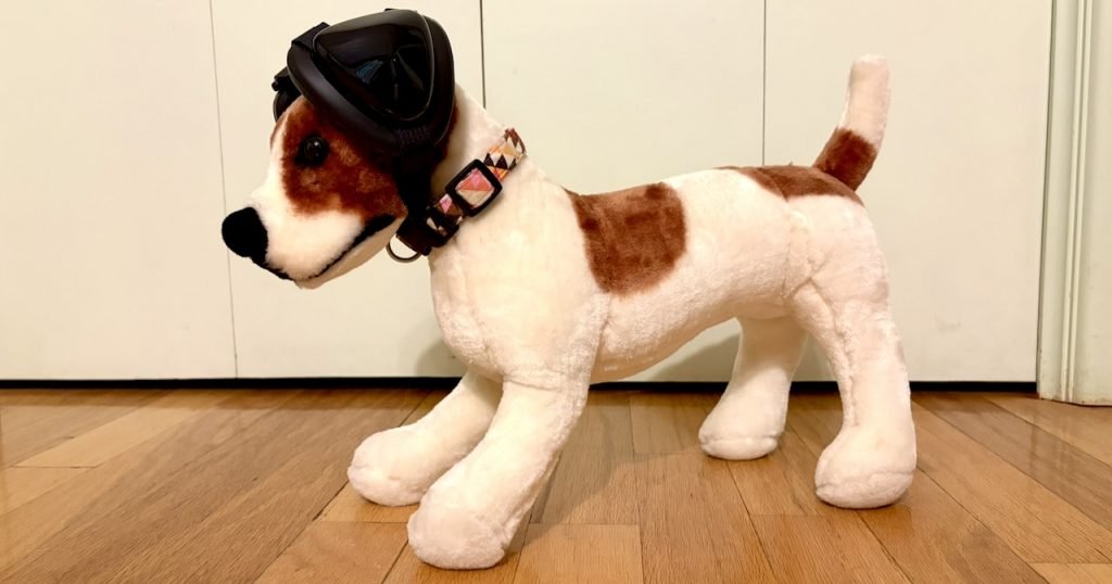 A standing brown and white stuffed dog wears Mutt Muffs ear protection