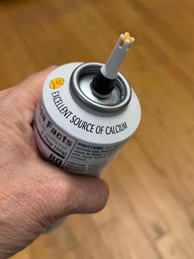 A closeup of the nozzle of a can of spray cheese with a little "cheese" showing