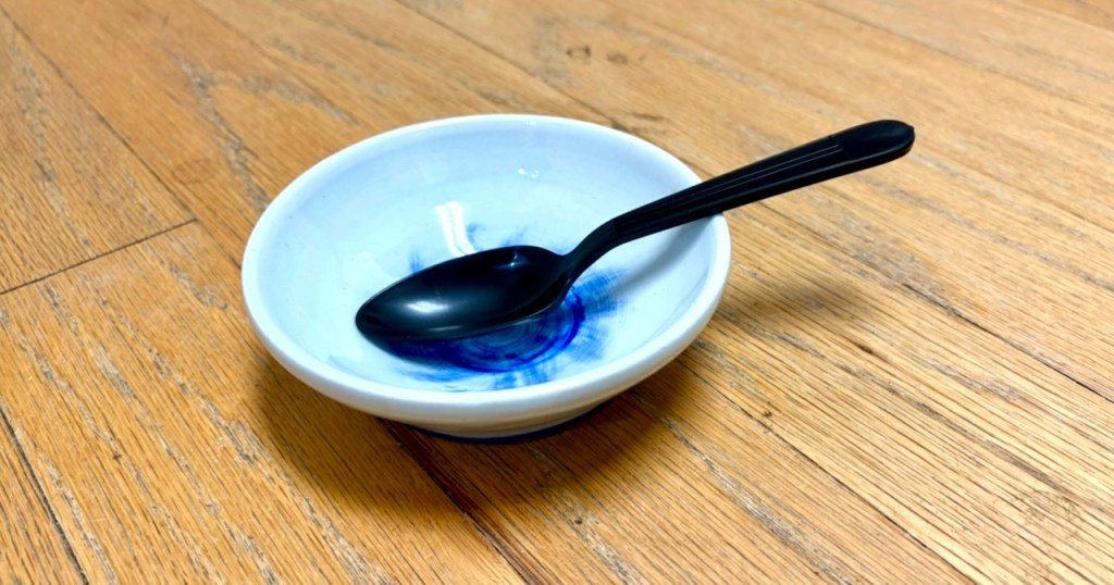 A small, white bowl with a black plastic spoon