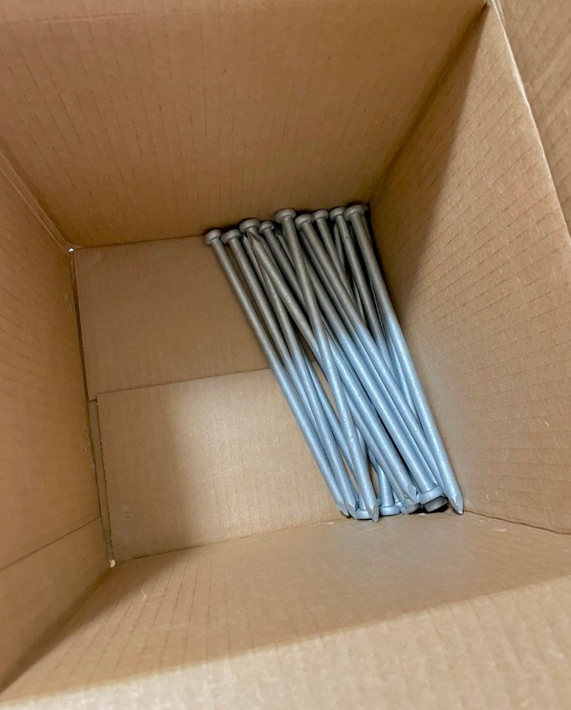 Looking down into a cardboard box with about a dozen metal stakes in it