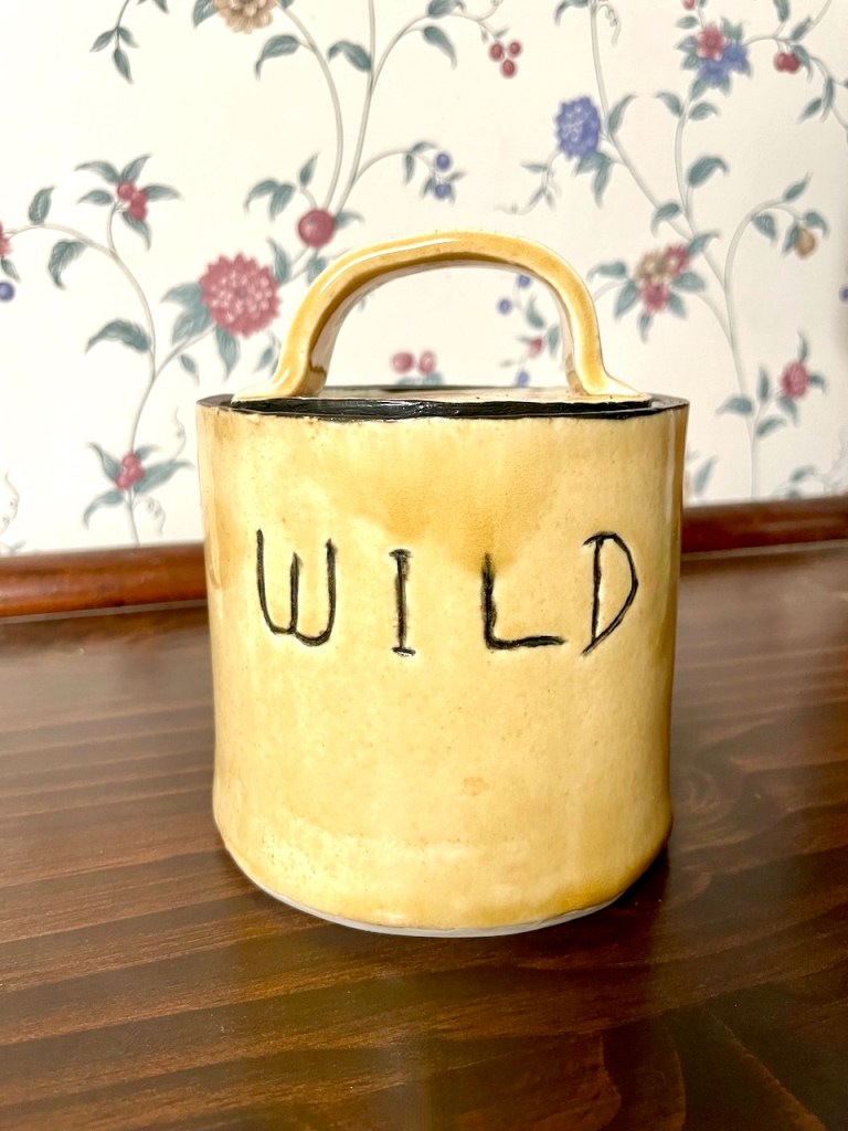 A ceramic treat jar that is a sandy yellow color with the word Wild inscribed in black